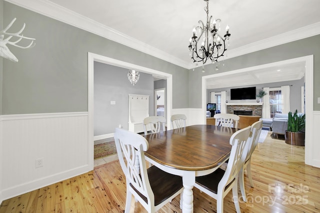 dining space featuring crown molding, light wood-type flooring, a notable chandelier, and a stone fireplace