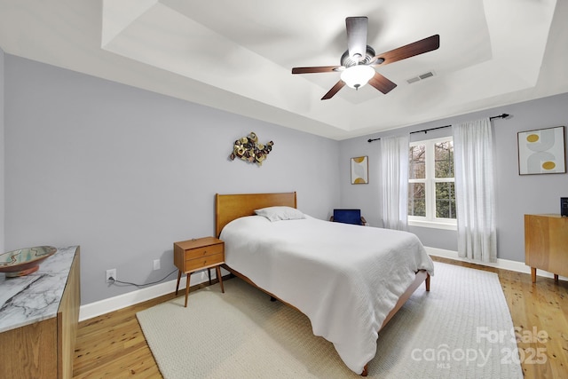 bedroom featuring ceiling fan, a tray ceiling, and light hardwood / wood-style flooring