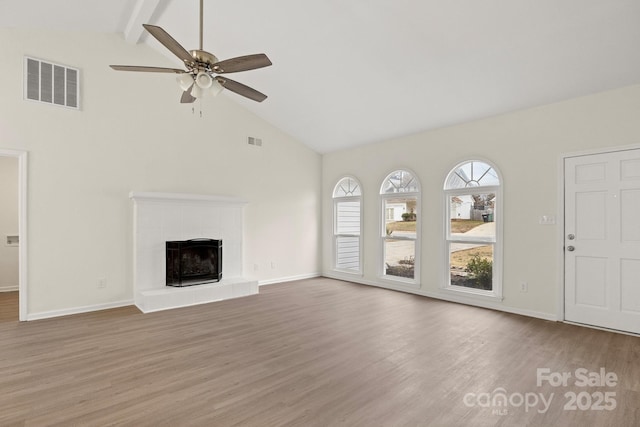 unfurnished living room with ceiling fan, a tile fireplace, beamed ceiling, hardwood / wood-style flooring, and high vaulted ceiling