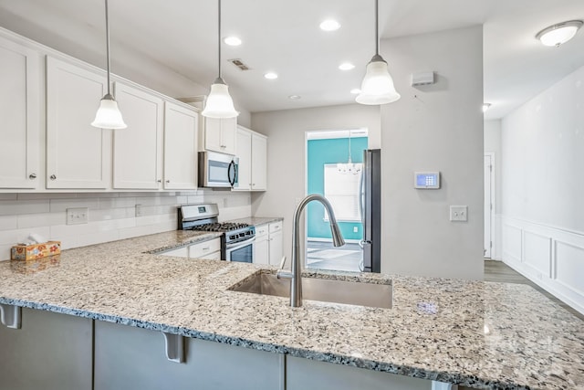 kitchen featuring white cabinets, appliances with stainless steel finishes, decorative light fixtures, sink, and kitchen peninsula