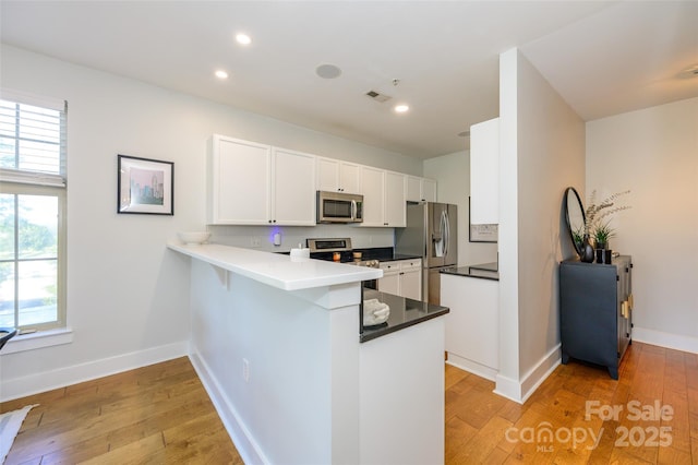 kitchen featuring white cabinetry, stainless steel appliances, tasteful backsplash, light hardwood / wood-style floors, and kitchen peninsula