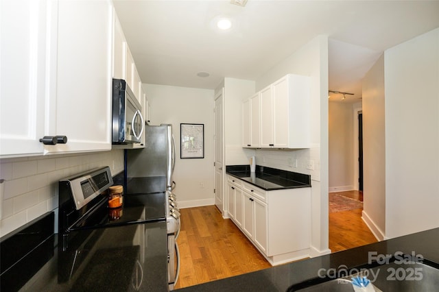 kitchen featuring appliances with stainless steel finishes, light hardwood / wood-style floors, white cabinetry, and tasteful backsplash