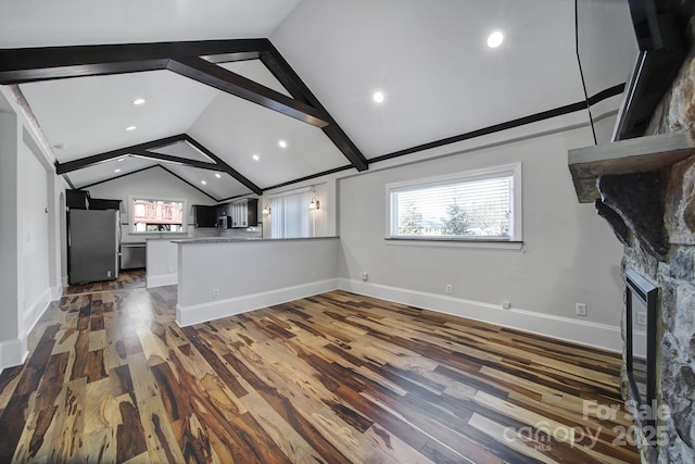 unfurnished living room with dark wood-type flooring, a stone fireplace, and vaulted ceiling with beams