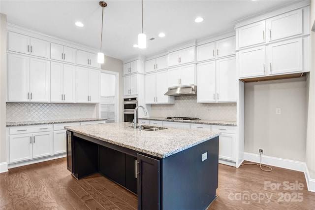 kitchen with pendant lighting, white cabinetry, an island with sink, sink, and light stone counters