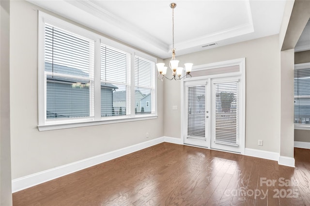 unfurnished dining area with a chandelier, a raised ceiling, ornamental molding, and dark hardwood / wood-style floors