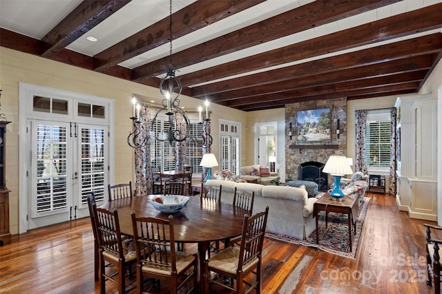 dining area with wood-type flooring, a wealth of natural light, beam ceiling, and a fireplace