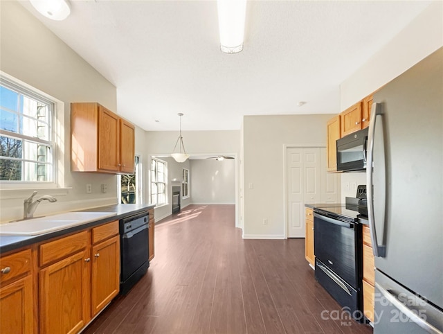 kitchen with pendant lighting, black appliances, dark wood-type flooring, sink, and ceiling fan