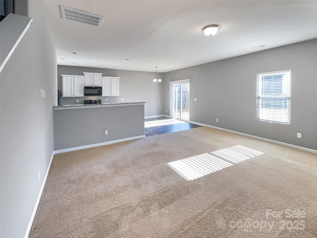 unfurnished living room featuring light carpet, plenty of natural light, and a notable chandelier