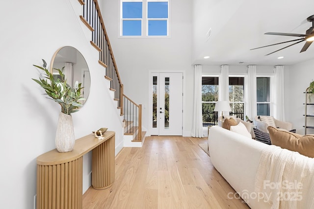 foyer with a towering ceiling, french doors, ceiling fan, and light wood-type flooring