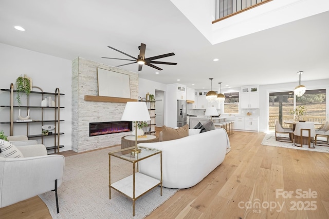 living room featuring ceiling fan, a stone fireplace, and light hardwood / wood-style flooring