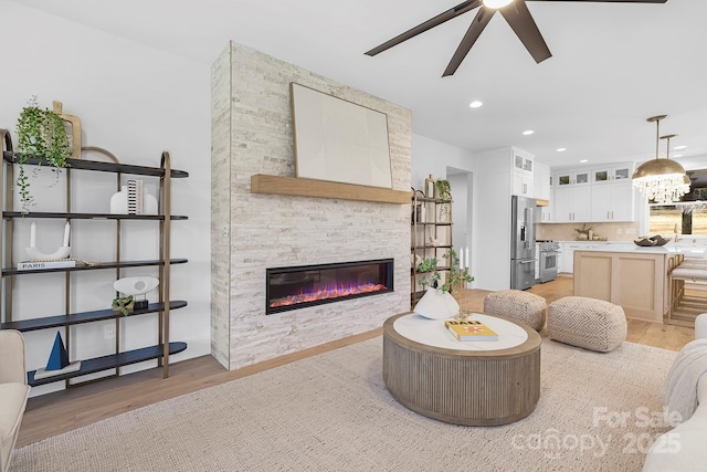 living room featuring a stone fireplace, ceiling fan with notable chandelier, and light hardwood / wood-style flooring