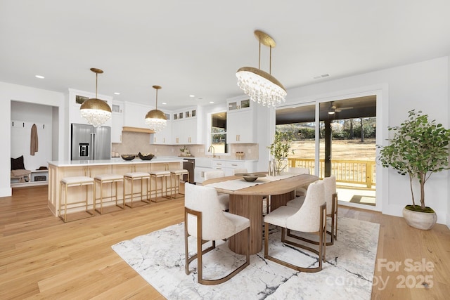 dining space featuring ceiling fan with notable chandelier, sink, and light hardwood / wood-style floors