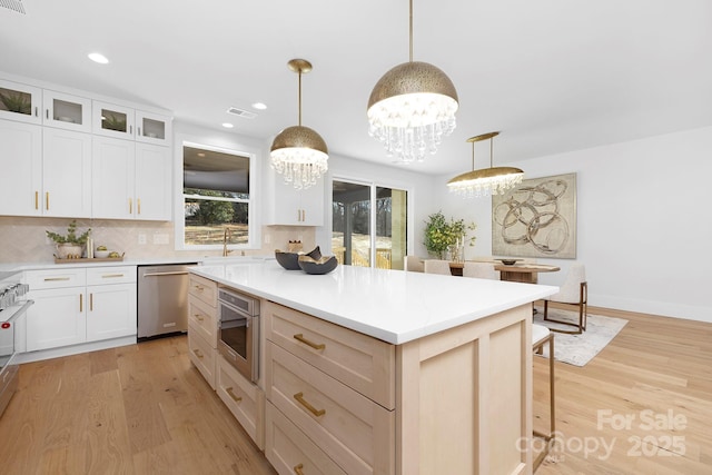 kitchen featuring decorative light fixtures, a center island, light wood-type flooring, dishwasher, and backsplash