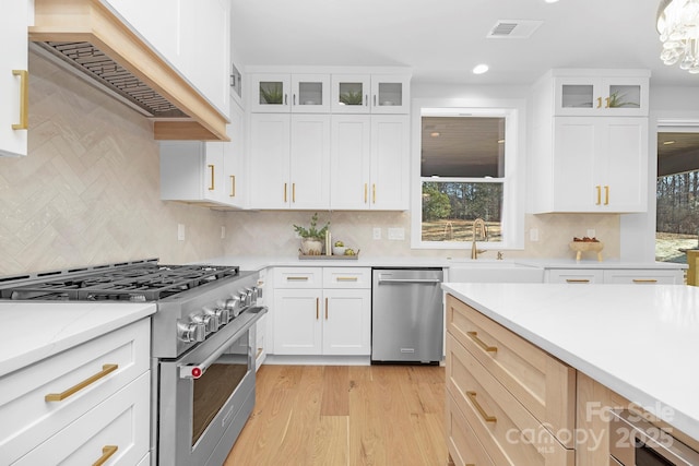 kitchen featuring stainless steel appliances, white cabinetry, custom exhaust hood, and light hardwood / wood-style floors