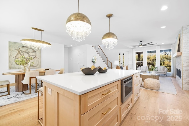 kitchen featuring a large fireplace, decorative light fixtures, light brown cabinetry, and light wood-type flooring