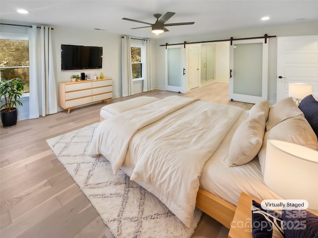 bedroom featuring ceiling fan, light hardwood / wood-style floors, and a barn door