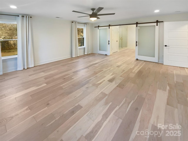 unfurnished room featuring ceiling fan, light hardwood / wood-style flooring, and a barn door