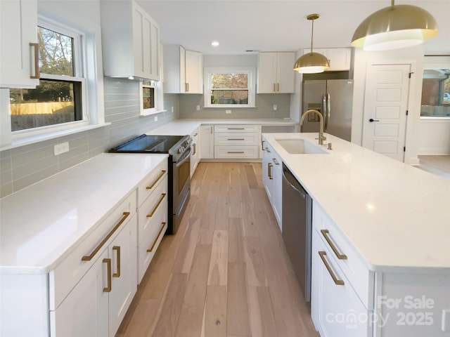 kitchen featuring sink, hanging light fixtures, stainless steel appliances, and an island with sink