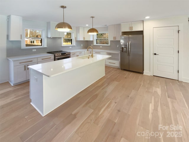 kitchen with appliances with stainless steel finishes, white cabinets, a center island with sink, and hanging light fixtures