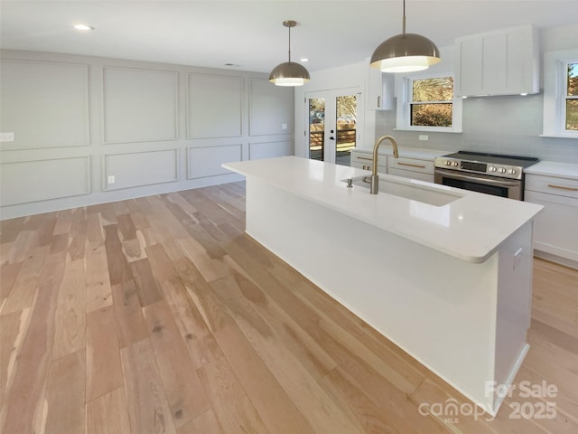 kitchen with electric range, sink, white cabinetry, hanging light fixtures, and an island with sink