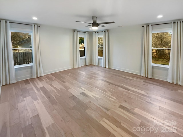 empty room with ceiling fan, a wealth of natural light, and light hardwood / wood-style floors