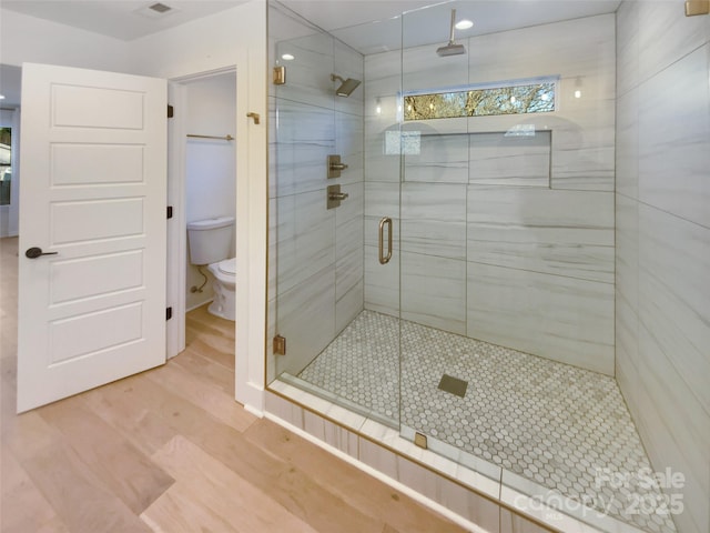 bathroom featuring toilet, hardwood / wood-style flooring, and a shower with door