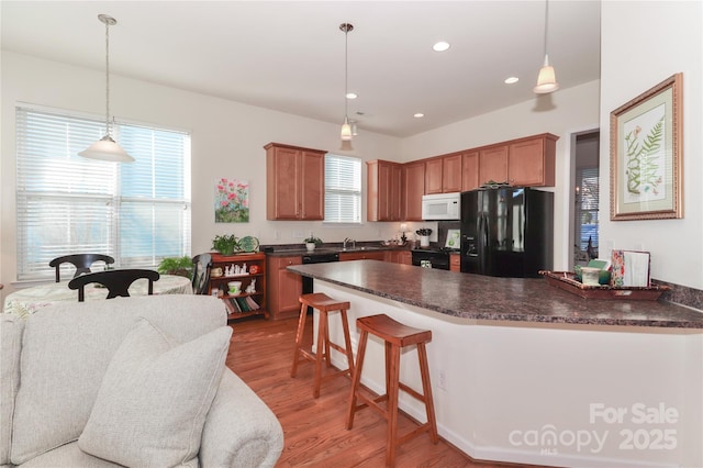 kitchen featuring decorative light fixtures, a breakfast bar, hardwood / wood-style floors, and black appliances