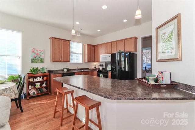 kitchen with kitchen peninsula, decorative light fixtures, light wood-type flooring, black appliances, and sink