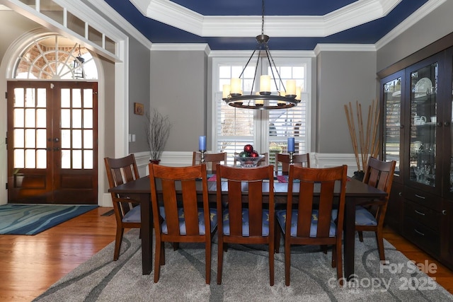 dining space with a tray ceiling, an inviting chandelier, hardwood / wood-style flooring, ornamental molding, and french doors