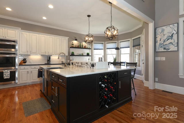 kitchen with decorative light fixtures, an inviting chandelier, white cabinetry, an island with sink, and dark hardwood / wood-style flooring