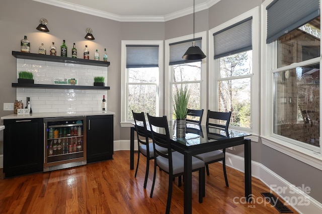 dining room with a wealth of natural light, beverage cooler, ornamental molding, and bar