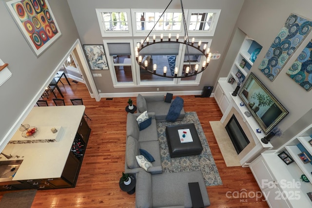 living room with built in shelves, a towering ceiling, hardwood / wood-style floors, and a notable chandelier