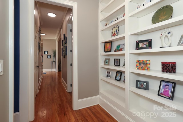 hallway with dark hardwood / wood-style flooring, crown molding, and built in features