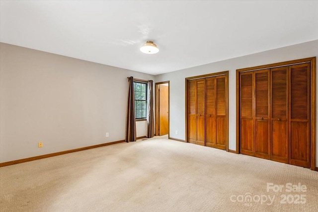 unfurnished bedroom featuring two closets and light colored carpet