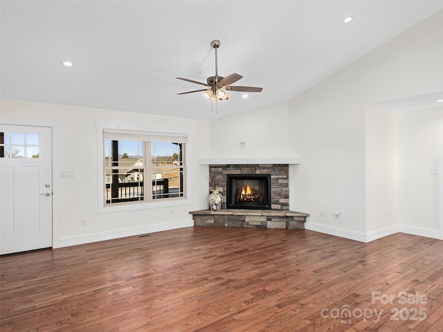 unfurnished living room featuring ceiling fan, dark hardwood / wood-style flooring, a stone fireplace, and vaulted ceiling