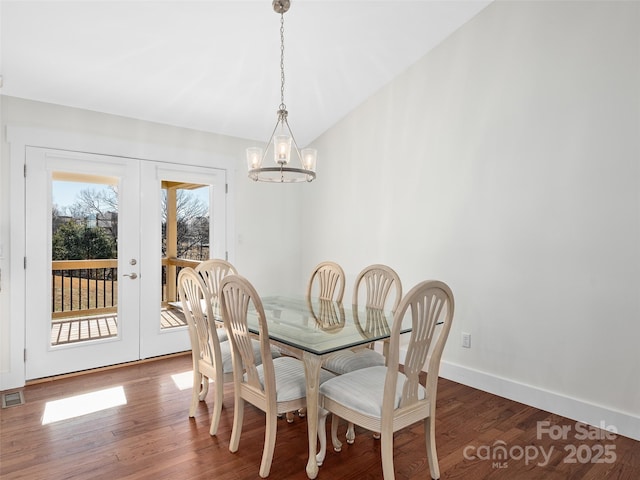 dining space featuring dark wood-type flooring, lofted ceiling, french doors, and an inviting chandelier