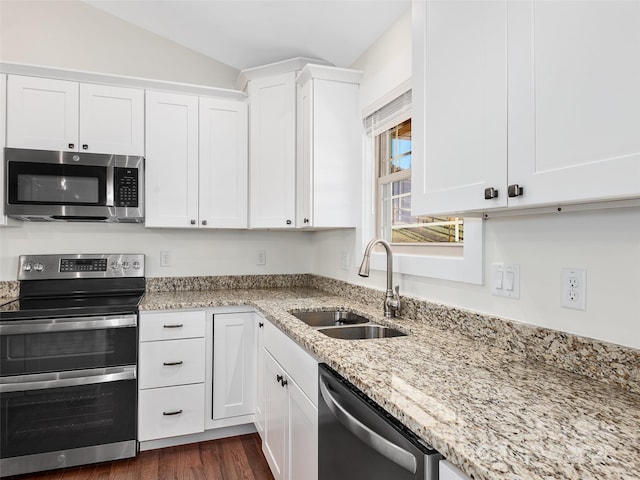 kitchen featuring white cabinetry, stainless steel appliances, vaulted ceiling, light stone counters, and sink