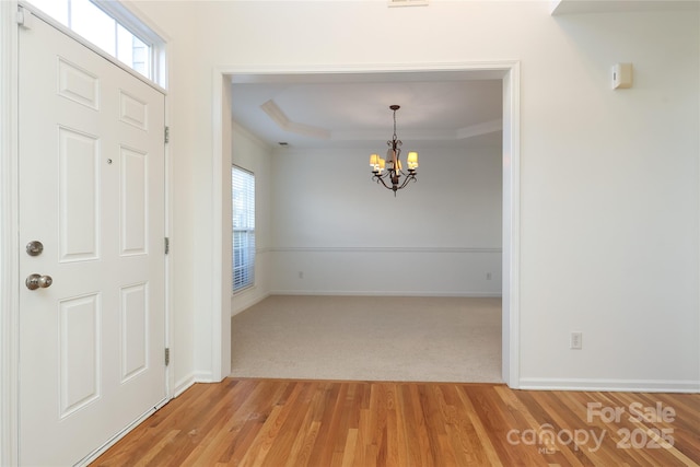 foyer with an inviting chandelier, a wealth of natural light, a tray ceiling, and hardwood / wood-style floors