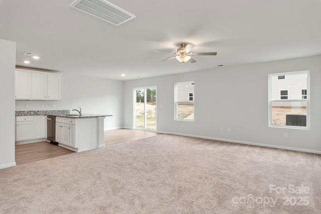 unfurnished living room with ceiling fan, light colored carpet, and sink