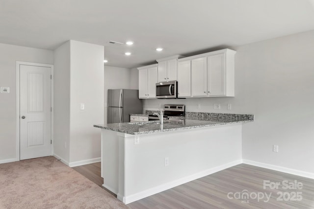 kitchen featuring kitchen peninsula, sink, white cabinetry, appliances with stainless steel finishes, and stone countertops