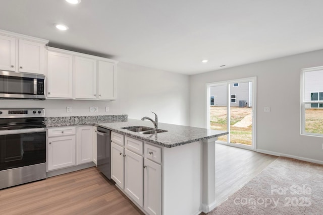 kitchen with light stone countertops, white cabinets, stainless steel appliances, sink, and kitchen peninsula