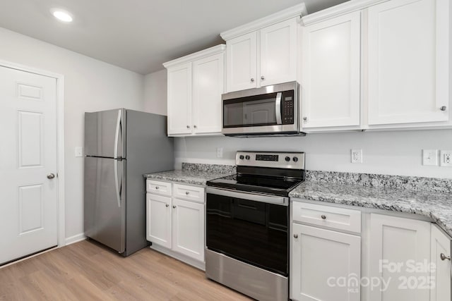 kitchen with light stone counters, white cabinets, appliances with stainless steel finishes, and light hardwood / wood-style flooring