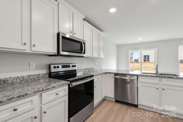 kitchen with appliances with stainless steel finishes, white cabinetry, sink, light stone counters, and light hardwood / wood-style flooring