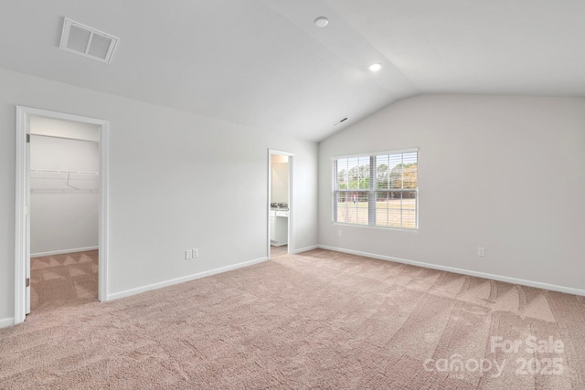 unfurnished bedroom featuring a spacious closet, a closet, vaulted ceiling, light colored carpet, and ensuite bathroom