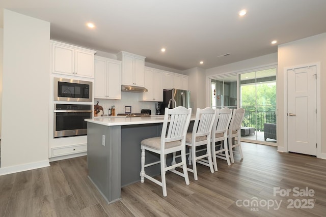 kitchen featuring a breakfast bar area, a kitchen island with sink, appliances with stainless steel finishes, and white cabinetry