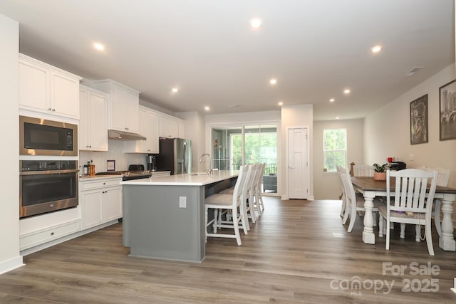 kitchen featuring a breakfast bar, white cabinetry, appliances with stainless steel finishes, and a center island with sink