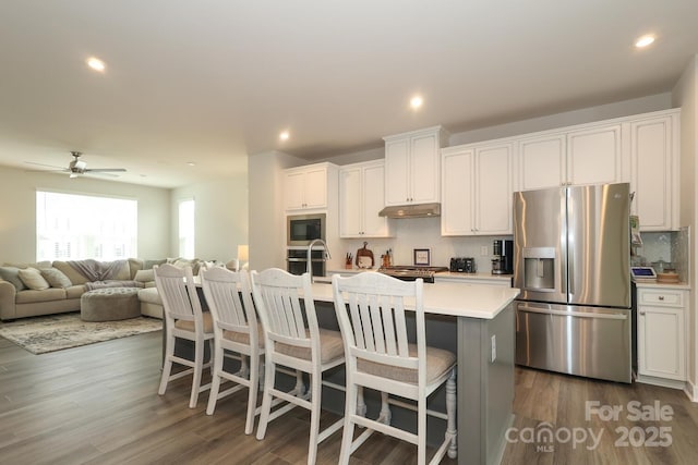 kitchen with ceiling fan, a kitchen island with sink, appliances with stainless steel finishes, and white cabinetry