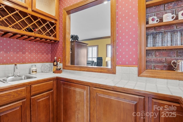 kitchen featuring a sink, brown cabinets, tile counters, and wallpapered walls