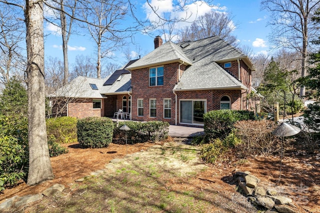 rear view of house featuring roof mounted solar panels, a shingled roof, brick siding, a chimney, and a patio area