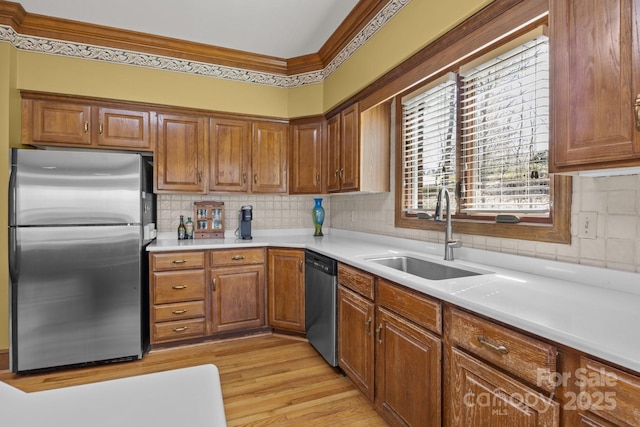 kitchen featuring brown cabinets, light wood-style flooring, ornamental molding, a sink, and appliances with stainless steel finishes